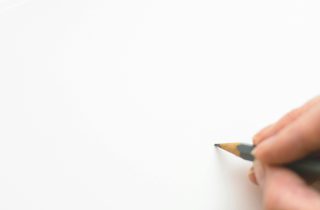 Close-up of a hand sketching on white paper with a pencil, emphasizing creativity.